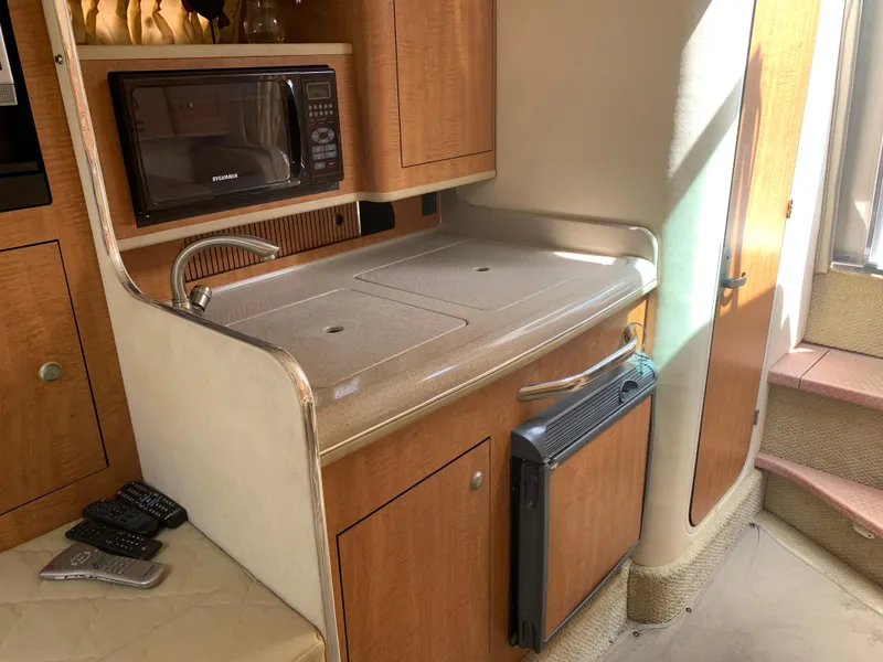 Slide: The Image of 2006 Sea Ray 280 Sundancer cabin kitchen with microwave, sink, and wooden cabinetry. - 14