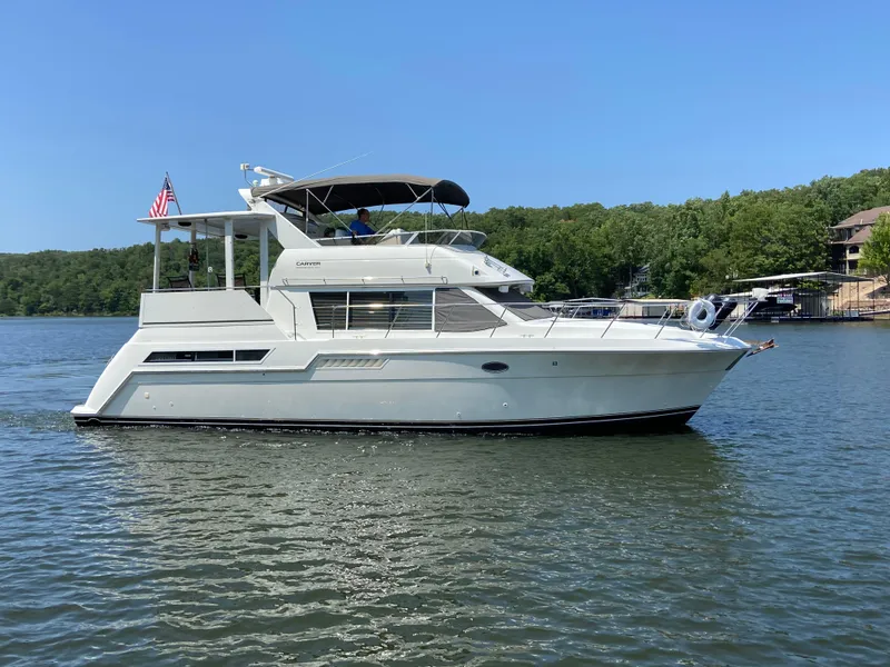 The Image of 1997 Carver 405 Motor Yacht cruising on a serene lake under a clear blue sky. - 0