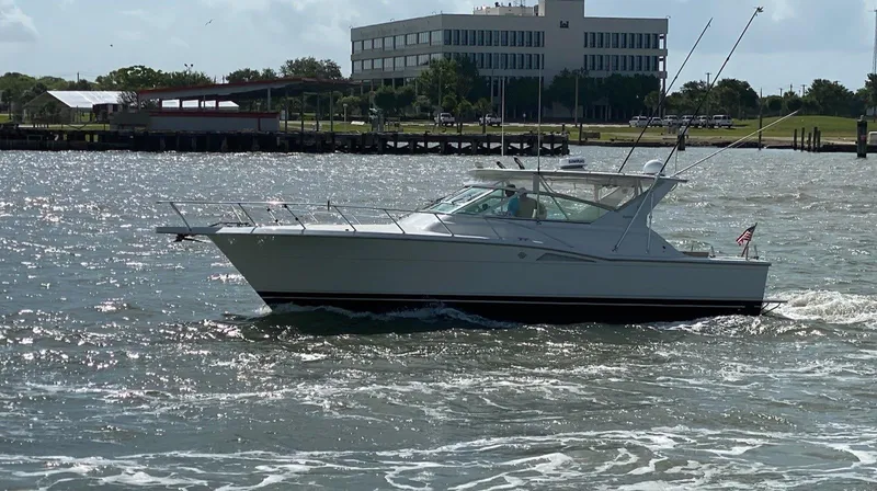 Slide: The Image of 1998 Hatteras 39 Sport Express boat cruising on a sunny day near a waterfront building. - 4
