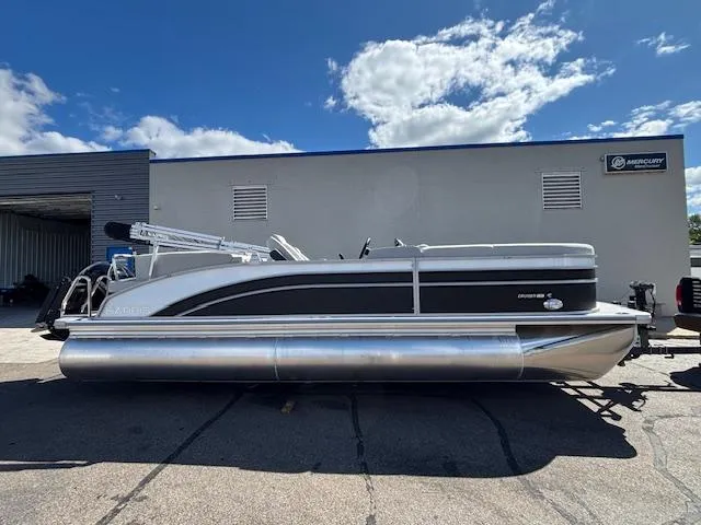 The Image of 2025 Harris Cruiser 230 pontoon boat parked outdoors under a partly cloudy sky. - 1