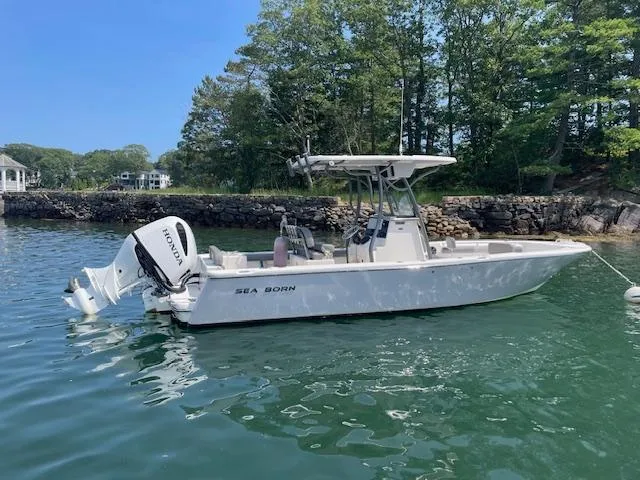 The Image of 2022 Sea Born LX24 Center Console boat on calm water near a stone wall. - 1
