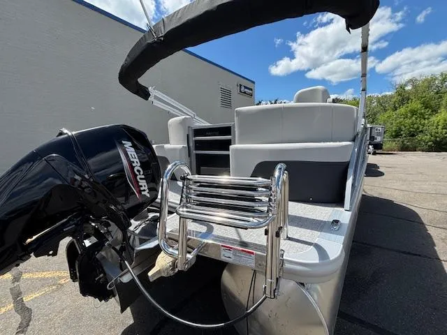 Slide: The Image of 2025 Harris Cruiser 190 boat with Mercury engine and ladder, parked outdoors under blue sky. - 4