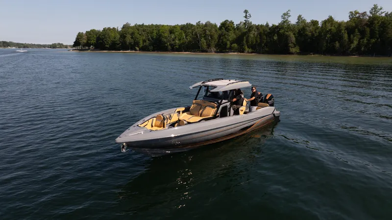 Slide: The Image of 2025 Sunsation 32 CCX boat cruising on a serene lake with lush green shoreline. - 2