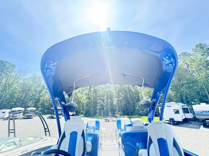 Slide: The Image of 2017 Manitou X-Plode Series 25 XT SRS SHP boat under bright sun, surrounded by trees and trailers. - 20