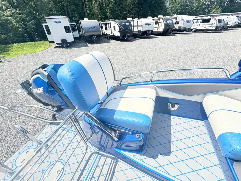 Slide: The Image of 2017 Manitou X-Plode Series 25 XT SRS SHP boat with blue and white seating, parked near RVs. - 24