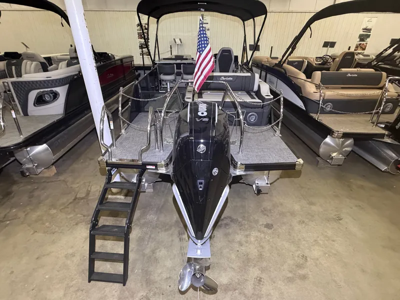 Slide: The Image of The image shows a 2026 Barletta Corsa 25 UE pontoon boat in a showroom. It features an American flag at the stern. - 34