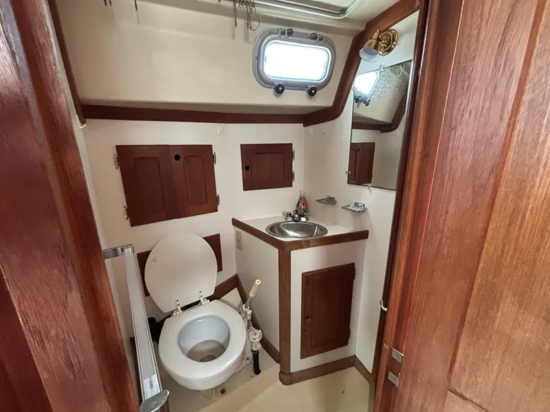 Slide: The Image of 1988 Bristol 33.3 yacht bathroom with wooden cabinets, toilet, sink, and porthole window. - 18