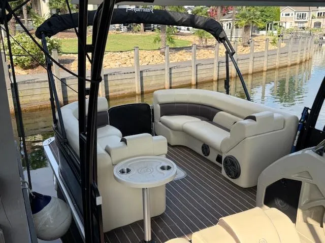 Slide: The Image of 2022 Premier 250 Sunsation pontoon boat with luxurious seating and table, docked by a scenic waterfront. - 9