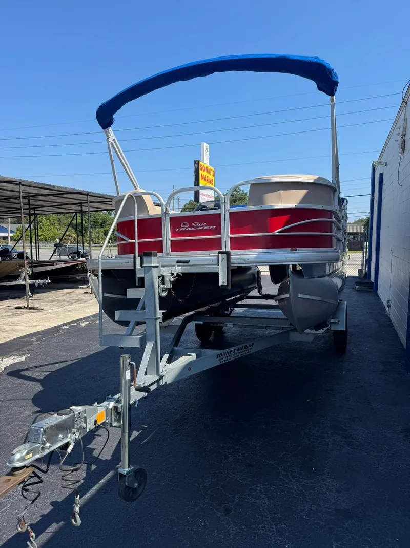 Slide: The Image of 2017 Sun Tracker Party Barge 20 DLX pontoon boat on trailer, blue canopy, parked outdoors. - 2