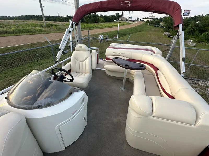 Slide: The Image of 2009 Bennington 2577RFi pontoon boat with beige seating and maroon canopy, parked near a fence. - 7