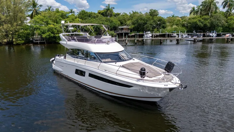 Slide: The Image of 2018 Prestige 500 Flybridge yacht cruising on a serene river with lush greenery. - 2