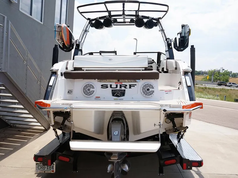 Slide: The Image of 2022 Cobalt R6 Surf boat rear view, parked on a trailer near a building. - 19