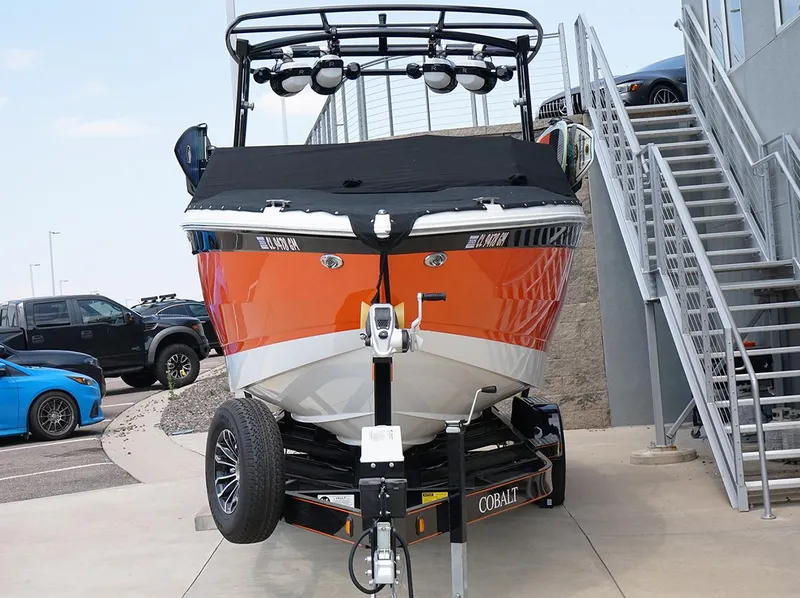 Slide: The Image of 2022 Cobalt R6 Surf boat in orange, parked on a trailer near stairs. - 4