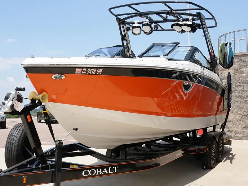 Slide: The Image of 2022 Cobalt R6 Surf boat on trailer, vibrant orange and white design, parked outdoors. - 5
