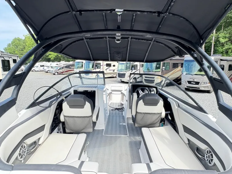Slide: The Image of 2019 Yamaha Boats 242 Limited E-Series interior with seating and dashboard, parked near RVs. - 10