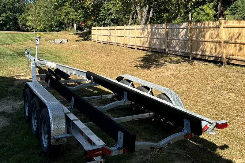Slide: The Image of Trailer for 2023 Sailfish 312 CC boat, parked on grass near wooden fence. - 19