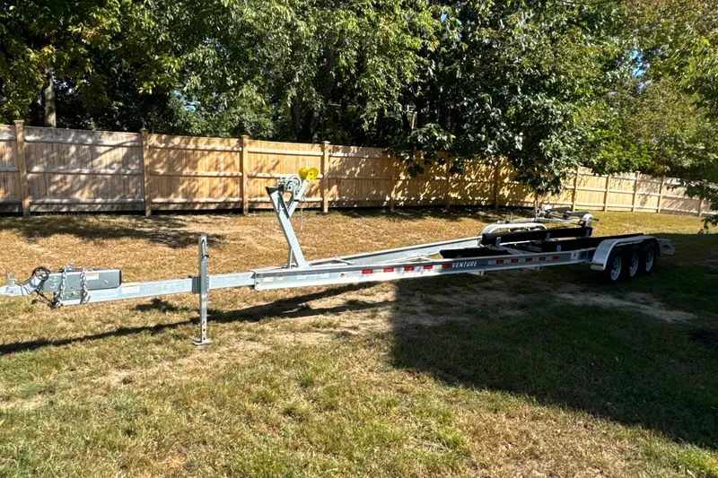 Slide: The Image of Trailer for 2023 Sailfish 312 CC boat parked on grass near wooden fence. - 20