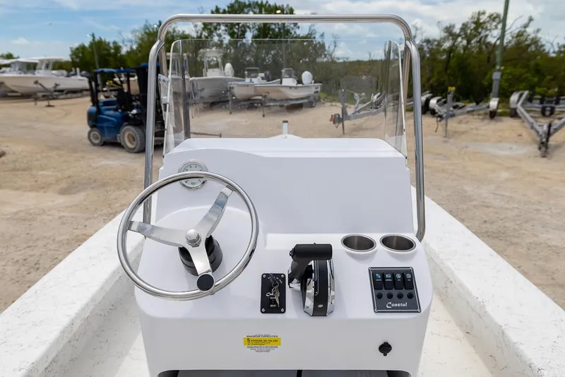 Slide: The Image of 2026 Coastal Skiff 231 boat console with steering wheel and controls, parked outdoors. - 7