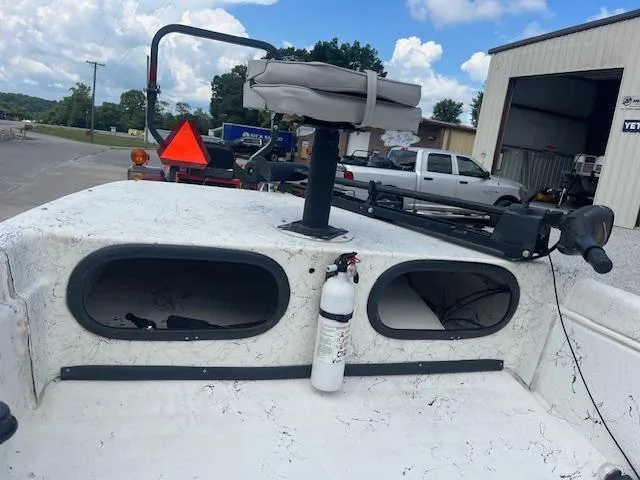 Slide: The Image of 2000 Carolina Skiff J1450 boat with mounted seat and fire extinguisher, parked near a garage. - 2