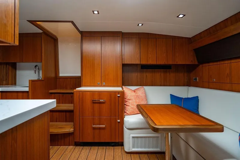 Slide: The Image of 2023 Hatteras GT45X yacht interior with wooden cabinetry, white seating, and colorful cushions. - 23