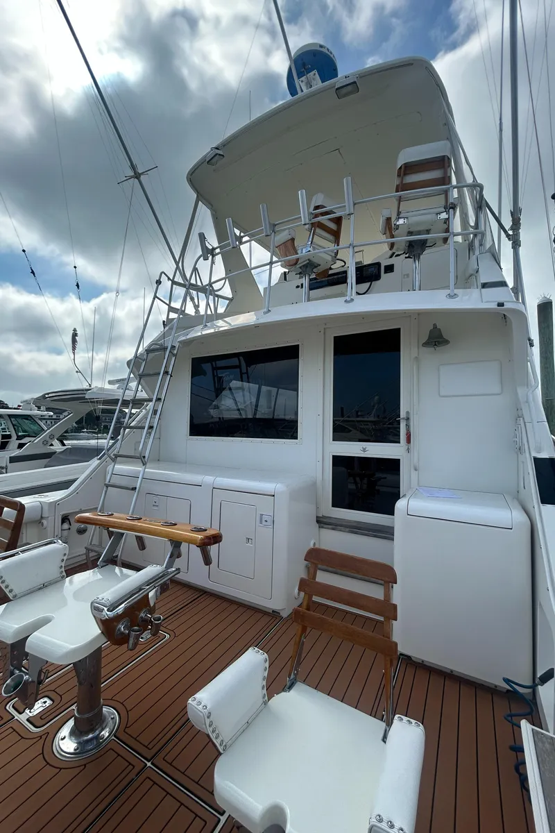 Slide: The Image of 1990 Bertram 50 Convertible yacht with wooden deck and seating, docked under cloudy skies. - 5