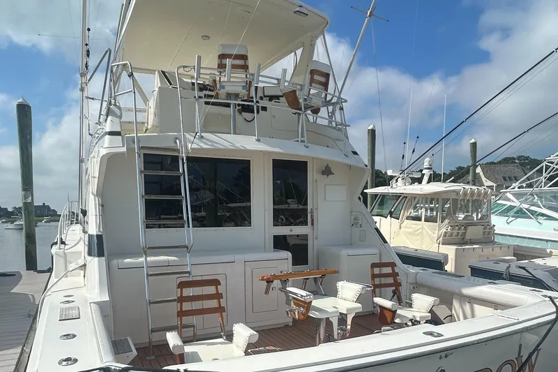 Slide: The Image of 1990 Bertram 50 Convertible yacht docked, featuring spacious deck and fishing chairs under a clear sky. - 6