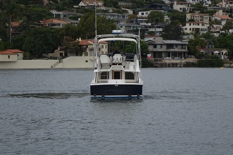 Slide: The Image of 1988 Blackfin 29 Flybridge boat on calm water, with scenic residential backdrop. - 11