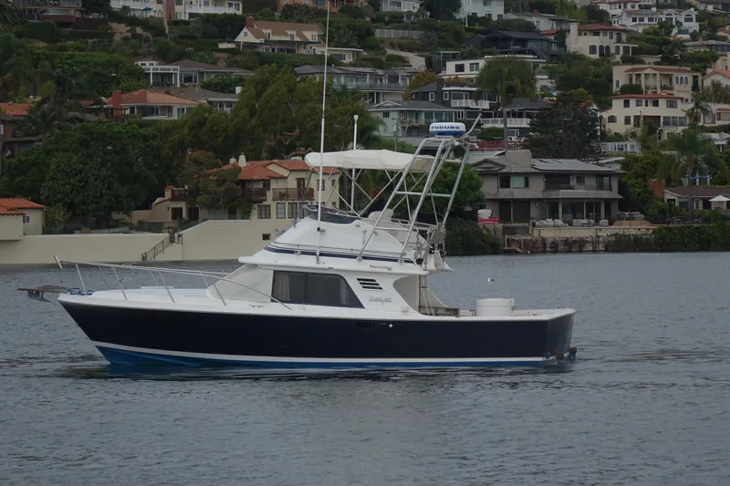 Slide: The Image of 1988 Blackfin 29 Flybridge boat on calm water near residential shoreline. - 2