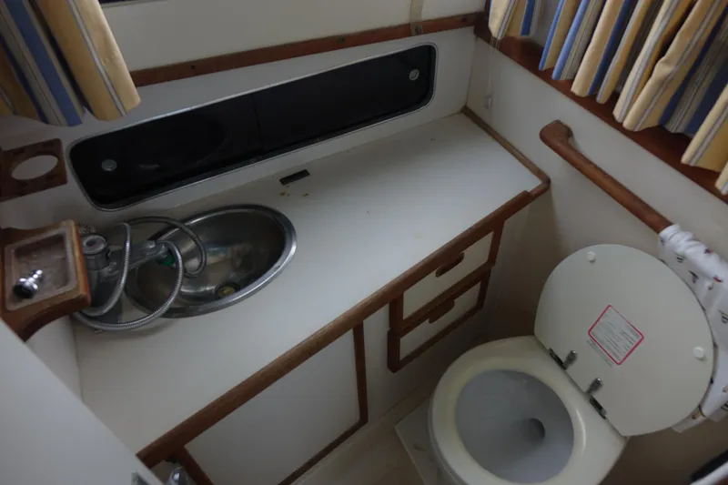 Slide: The Image of 1988 Blackfin 29 Flybridge boat bathroom with sink, toilet, and striped curtains. - 37