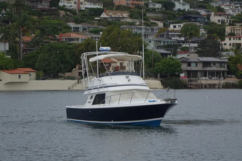 Slide: The Image of 1988 Blackfin 29 Flybridge boat cruising on a calm lake with houses in the background. - 7