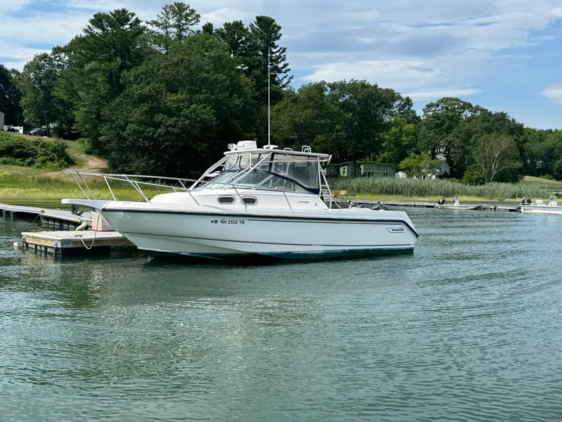 Slide: The Image of 1999 Boston Whaler 28 Conquest boat docked on calm water, surrounded by lush greenery. - 1