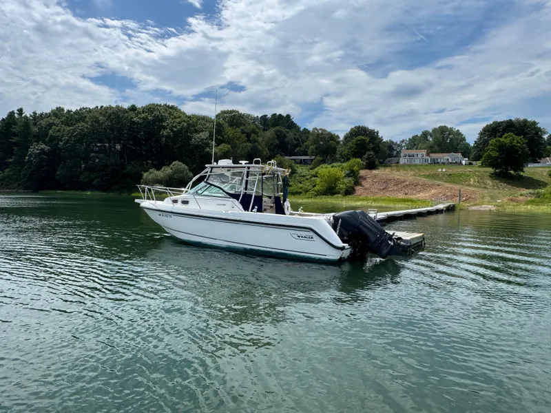 Slide: The Image of 1999 Boston Whaler 28 Conquest boat on calm water near a dock, surrounded by greenery. - 2