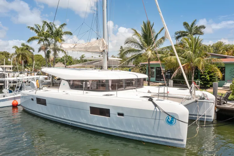 Slide: The Image of 2017 Lagoon 42 Owners Version catamaran docked near palm trees and waterfront homes. - 0