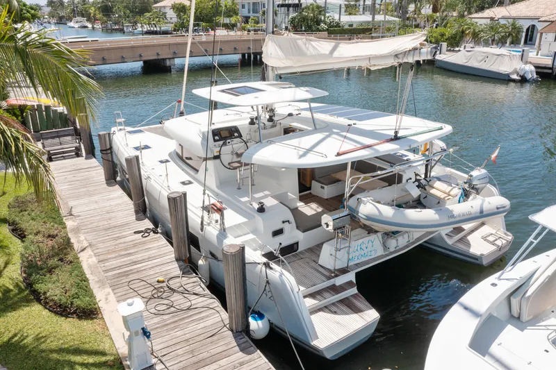 Slide: The Image of 2017 Lagoon 42 catamaran docked by tropical waterfront homes, surrounded by lush greenery. - 12