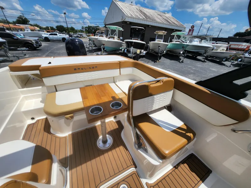 Slide: The Image of 2021 Bayliner VR6 Bowrider OB interior with tan seating and wooden table, parked outdoors. - 10