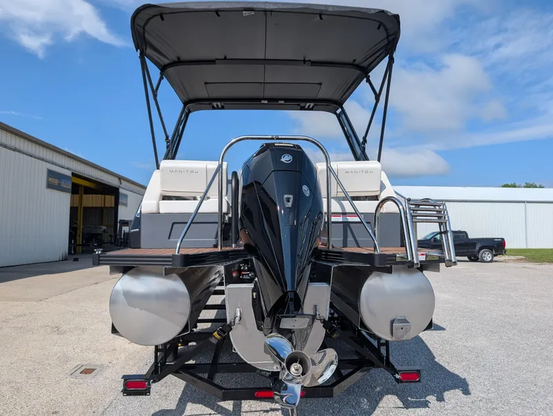 Slide: The Image of 2025 Manitou Explore pontoon boat with outboard motor, parked outdoors under a clear sky. - 3