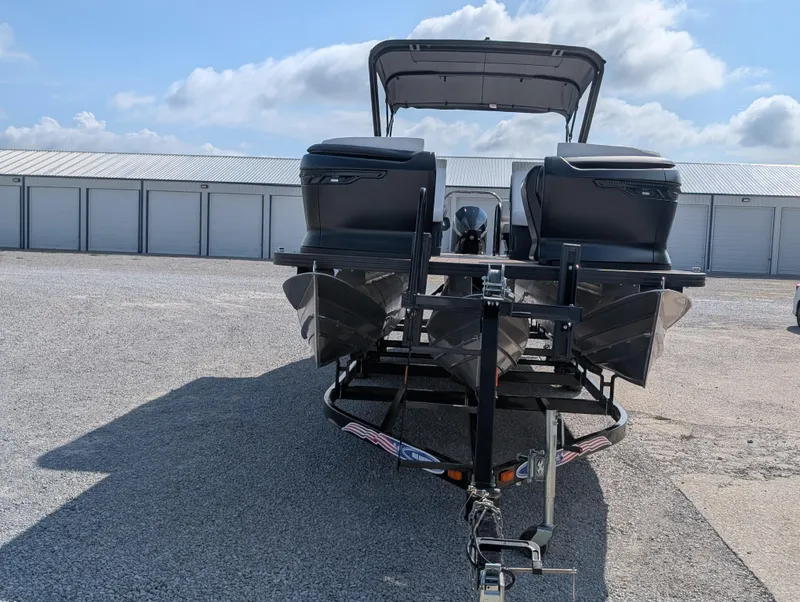 Slide: The Image of 2025 Manitou Explore boat on trailer, parked outdoors under a cloudy sky. - 8