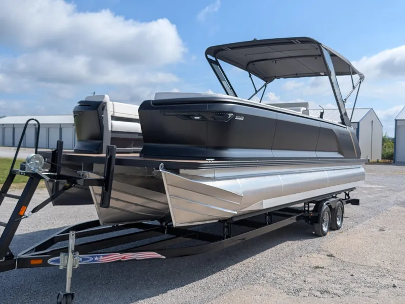 Slide: The Image of 2025 Manitou Explore pontoon boat on trailer, parked outdoors under a blue sky. - 9