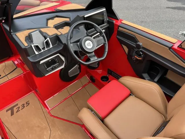 Slide: The Image of 2024 Axis Wake Research T235 boat interior with red and tan accents, modern dashboard, and steering wheel. - 6