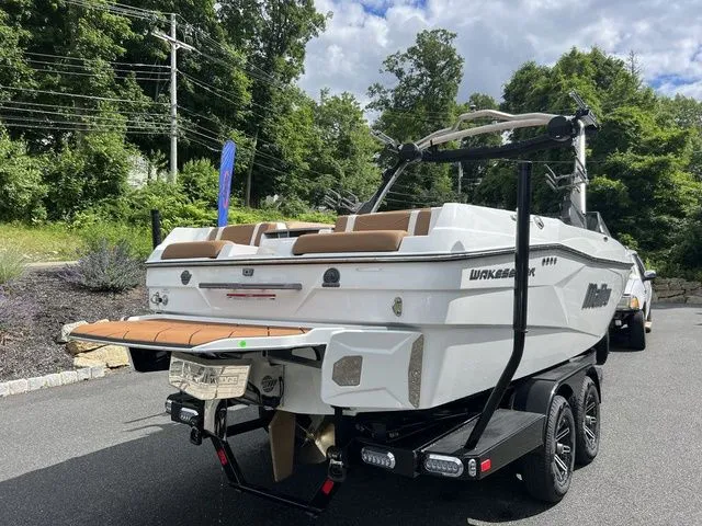 Slide: The Image of 2024 Malibu 23 LSV boat on trailer, parked outdoors, surrounded by trees and sky. - 10