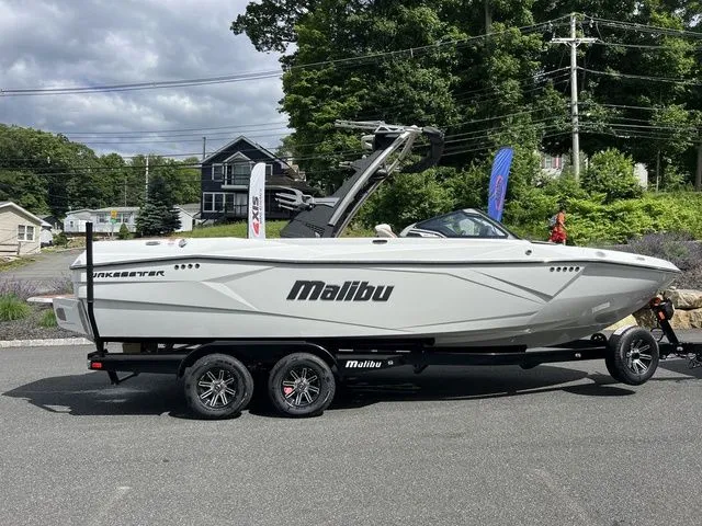 Slide: The Image of 2024 Malibu 23 LSV boat on trailer, parked outdoors with trees and houses in the background. - 3