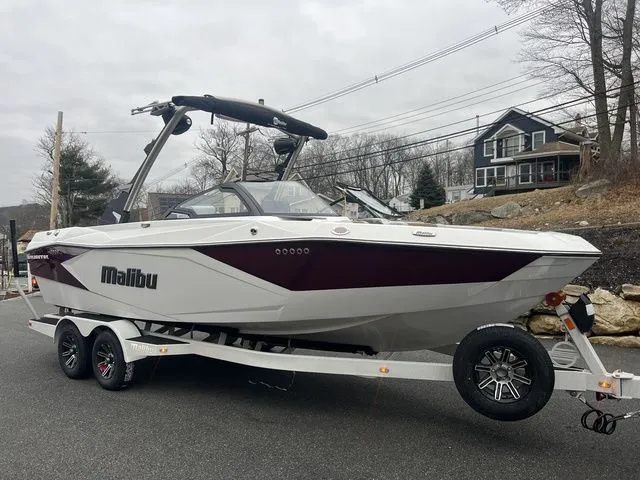 Slide: The Image of 2024 Malibu 23 LSV boat on trailer, parked on a road with houses in the background. - 6