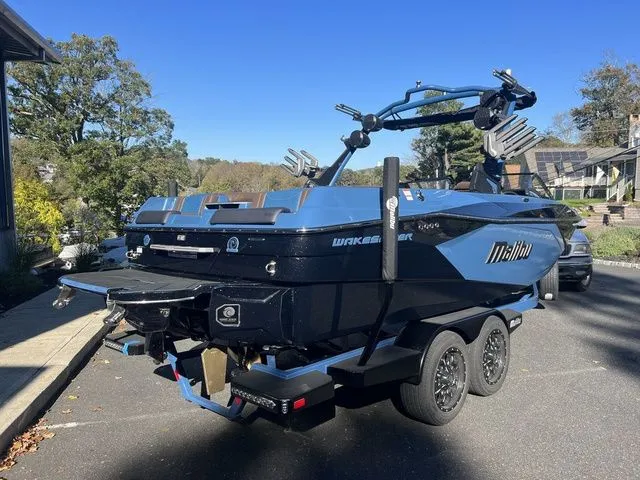Slide: The Image of 2024 Malibu 23 LSV boat on trailer, blue and black design, parked outdoors. - 3