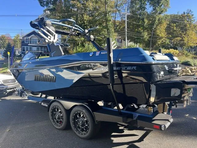 Slide: The Image of 2024 Malibu 23 LSV boat on trailer, parked outdoors with trees in background. - 5