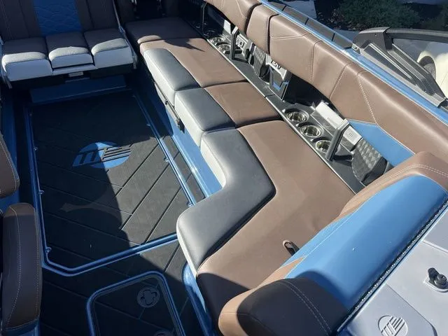 Slide: The Image of 2024 Malibu 23 LSV boat interior with brown and blue seating, cup holders, and logo floor mat. - 9