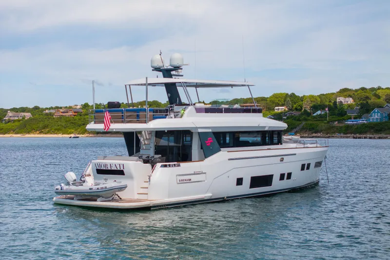 Slide: The Image of 2019 Sirena 64 yacht on calm water near a scenic shoreline. - 4