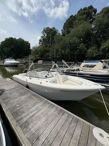 Slide: The Image of 2023 Cobia 220 Dual Console boat docked at a marina with lush trees in the background. - 4