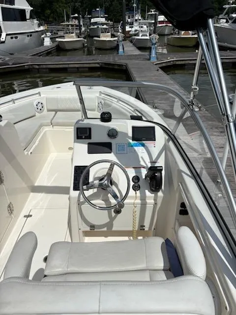 Slide: The Image of 2023 Cobia 220 Dual Console boat interior with steering wheel, dashboard, and docked marina view. - 6