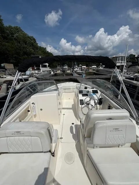 Slide: The Image of 2023 Cobia 220 Dual Console boat with white seating, docked under a blue sky. - 7