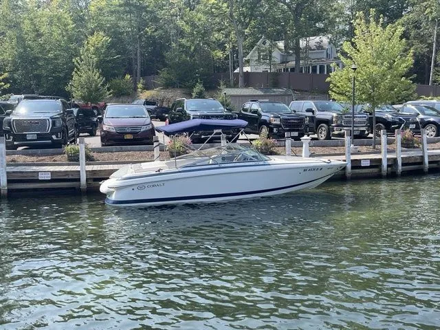 Slide: The Image of 2004 Cobalt 226 boat docked by waterfront with parked cars in background. - 1